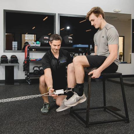 two men in a rehab clinic with one male doing leg exercises