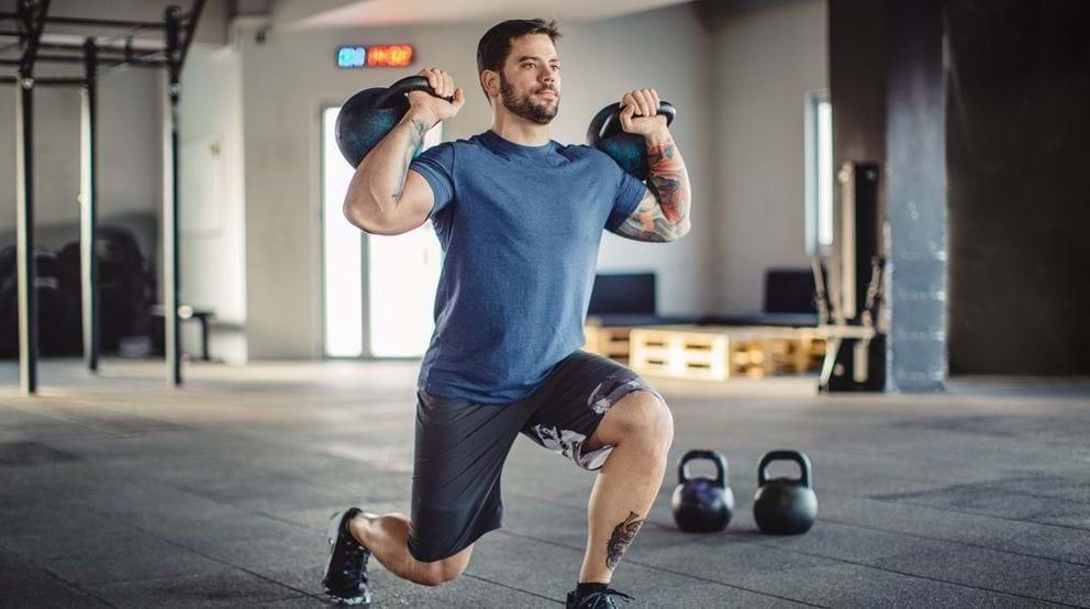 Muscly male holding kettlebells in a spacious gym